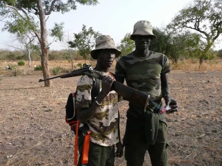 Un chasseur et son pisteur en brousse, arme à l’épaule