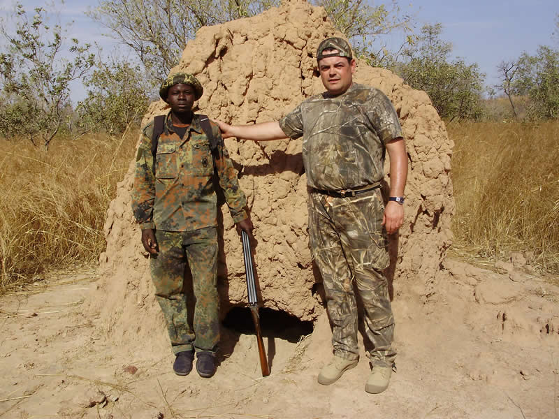 Un chasseur et son pisteur devant une termitière