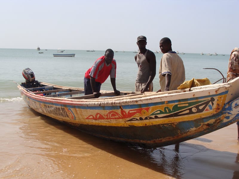Pêcheurs autour d’une pirogue peinte échouée sur la plage