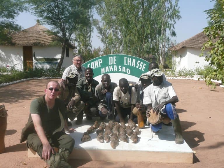 Chasseur et pisteurs devant l’enseigne du camp avec le tableau de la matinée